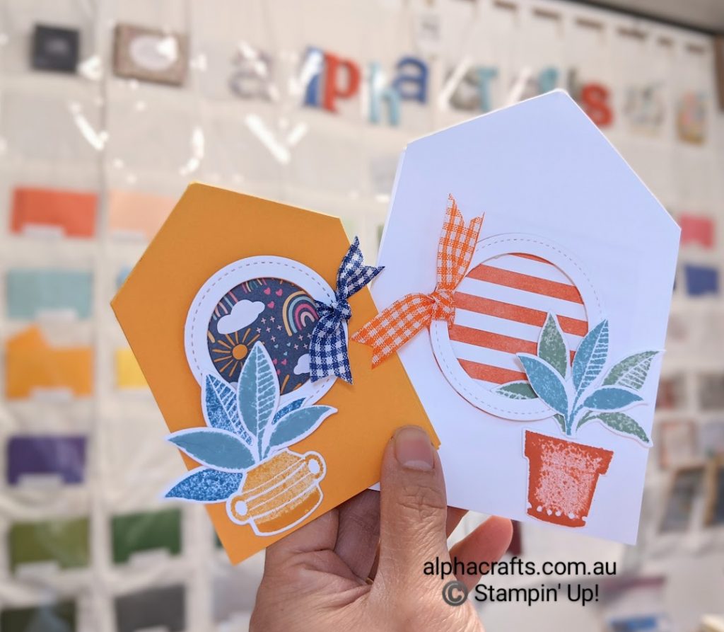 Cards shaped like paper houses. White card has a circle window frame with orange striped Designer Series Paper (DSP) and a potted plant. The orange card has a circle window frame with rainbow Designer Series Paper(DSP) and a potted plant.